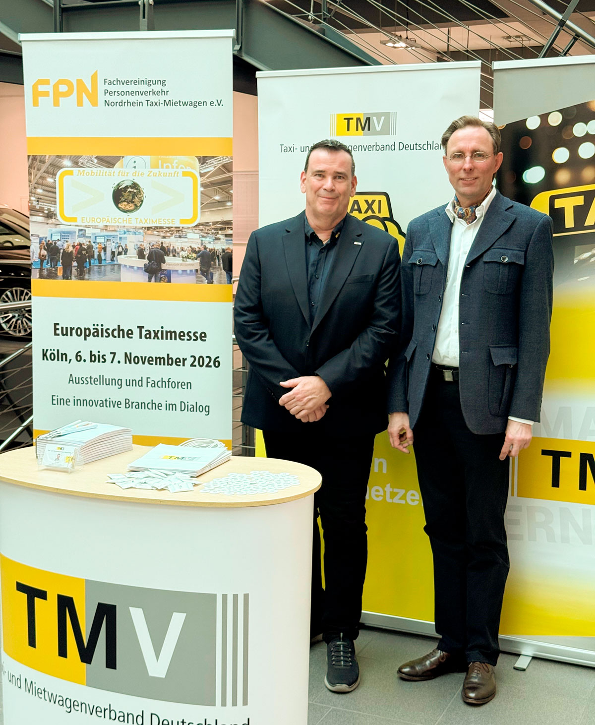 Nico Höttges und Dr. Michael Stehr stehen vor drei Roll-Ups der FPN und des TMV. Im Vordergrund ist eine Werbetheke des TMV zu sehen.